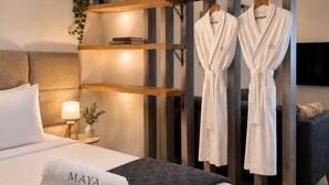 Une chambre d’hôtel moderne avec un lit, une table de chevet avec une lampe, une petite plante et deux peignoirs blancs suspendus à un porte-vêtements.