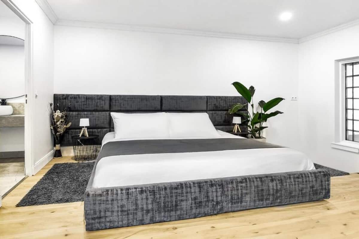 Ein modernes Schlafzimmer mit einem großen Bett, einem dunklen Kopfteil, einem Nachttisch mit einer Lampe und einer Topfpflanze.