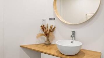 Une salle de bain avec un lavabo blanc, un plan de toilette en bois et un miroir rond.