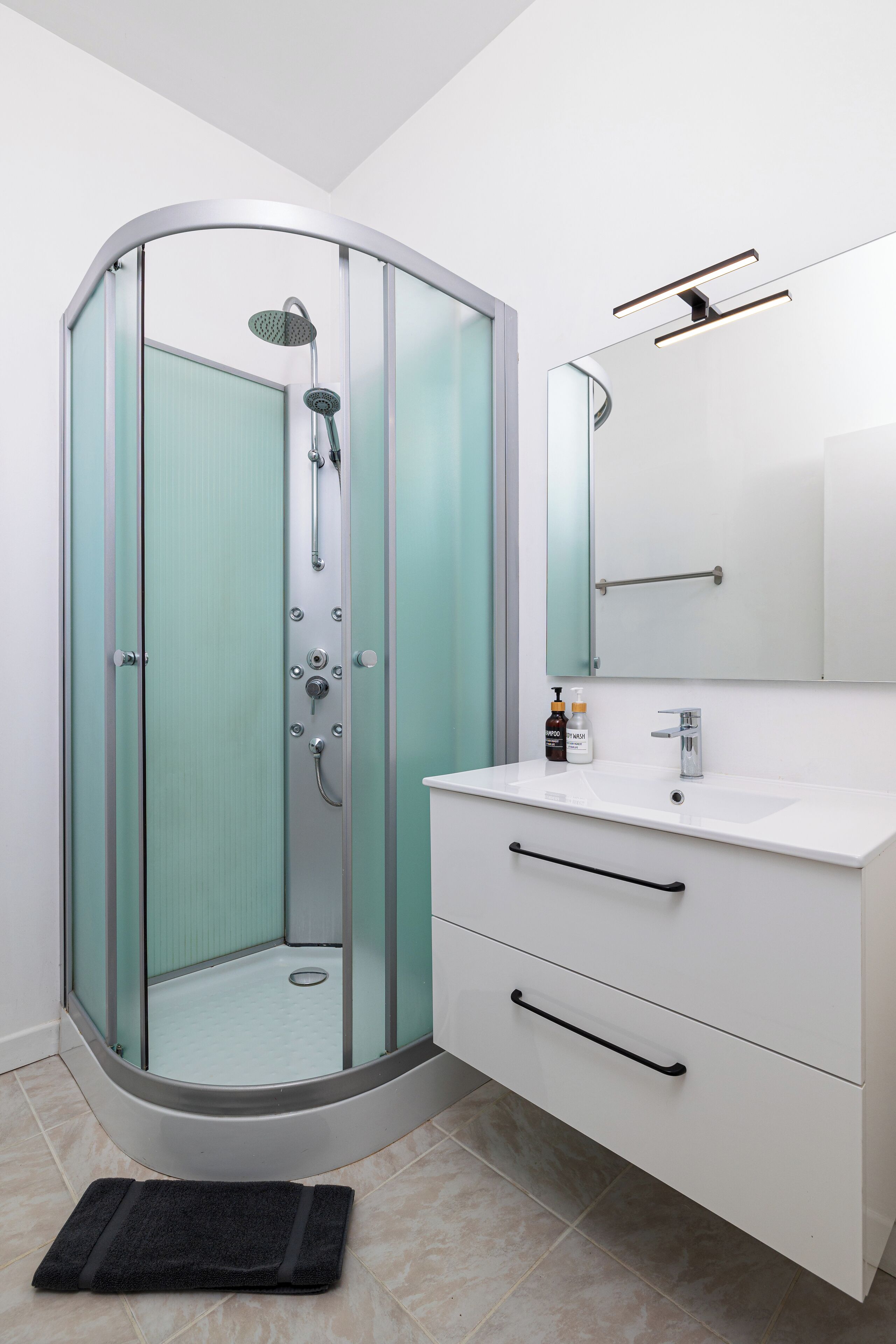 A modern bathroom with a glass-enclosed shower, a white sink, and a mirror above it.
