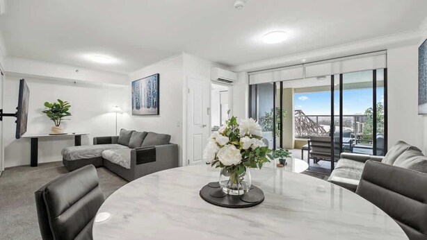 A modern living room with a round marble table, grey sofas, a glass coffee table, and a vase of white flowers. - The Executive! 1Bed, 1Bath, 1Car, VIEWS ~ CBD (Brisbane City)