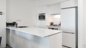 A modern kitchen with white cabinetry, a central island, a microwave, a stove, and a refrigerator. - The Executive! 1Bed, 1Bath, 1Car, VIEWS ~ CBD (Brisbane City)