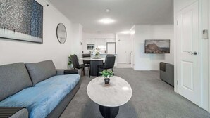 A modern living room with a grey sofa, a round coffee table, and a dining area with a white table and chairs. - The Executive! 1Bed, 1Bath, 1Car, VIEWS ~ CBD (Brisbane City)