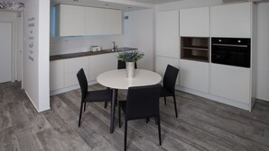 Une cuisine moderne avec des meubles blancs, une table de salle à manger ronde entourée de quatre chaises, une plante en pot et un four encastré.
