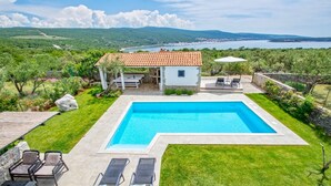 Une piscine dotée d’une pergola, d’un espace salon extérieur et offrant une vue sur un lac et des montagnes.
