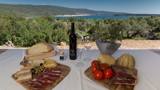 Une table dressée avec de la nourriture et du vin, une bouteille étiquetée « Sel et sable », et une vue panoramique sur un paysage côtier.