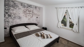 Una camera da letto con un letto, un comodino, una finestra con tende e una parete decorata.