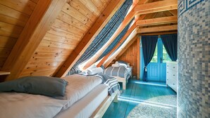 Ein Schlafzimmer mit schrägem Dach, einem Bett mit Kissen, einem Schminktisch und Blick durch eine Tür.