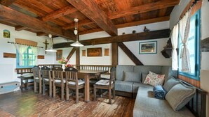 Ein rustikaler Innenraum mit freiliegenden Holzbalken, einem Holzesstisch mit Stühlen, einer Couch und einem Fenster mit Vorhängen.