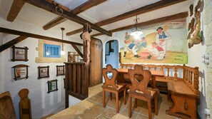 Un'area pranzo rustica con arredi in legno, pavimento in pietra e un affresco raffigurante una scena storica.