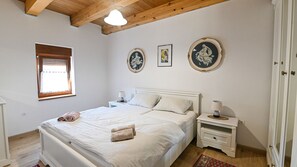 Een slaapkamer met een tweepersoonsbed, twee nachtkastjes, een raam met zonwering en drie ingelijste foto's aan de muur.