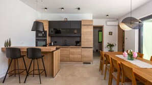 A modern kitchen with a central island, black bar stools, a wooden dining table with chairs, and pendant lighting. - Vila il Giardino Segreto with pool by Villas Guide (Matulji)