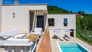 A modern outdoor pool area with lounge chairs and umbrellas, a wooden deck, and a view of a hillside. - Vila il Giardino Segreto with pool by Villas Guide (Matulji)