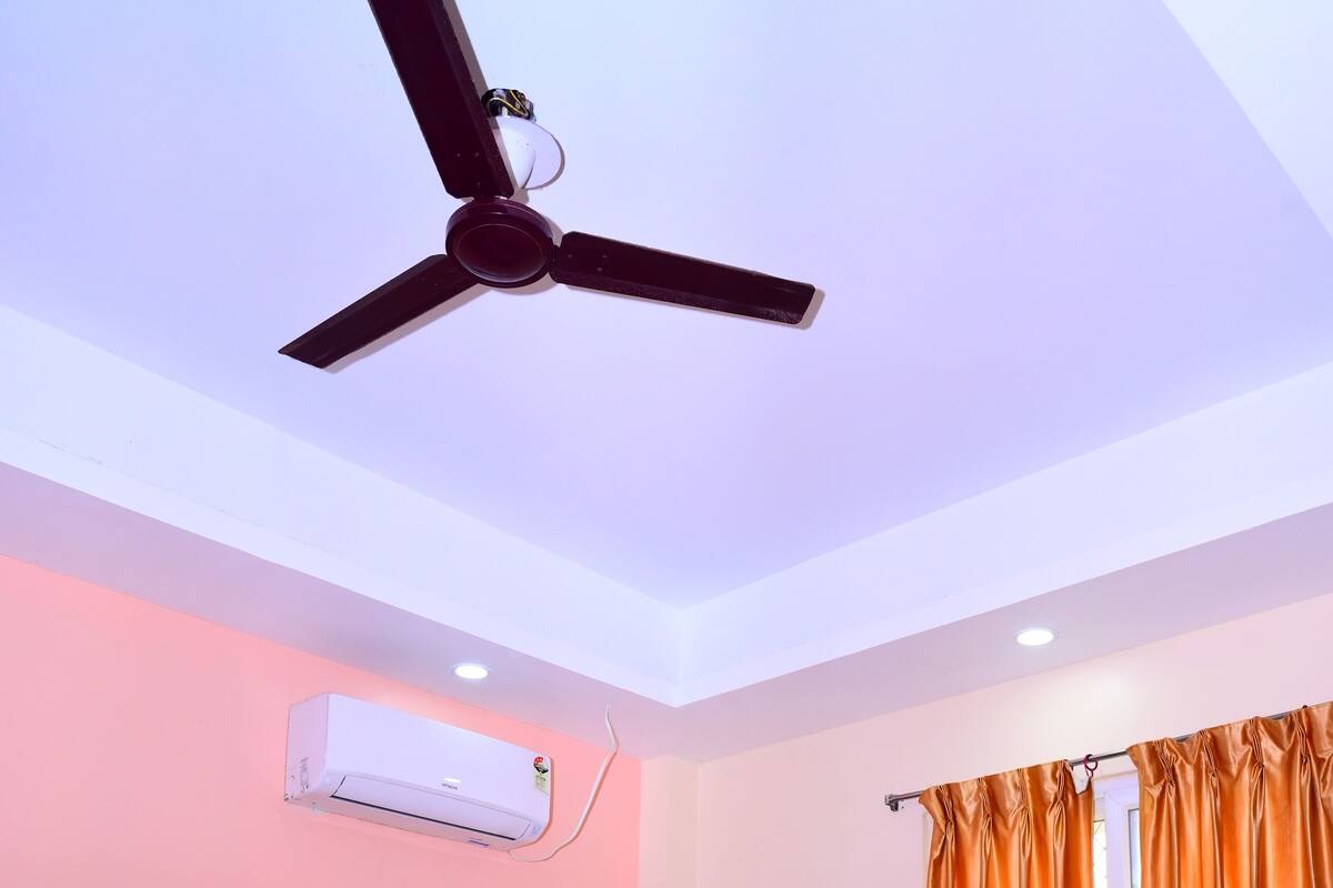 A hotel room with two beds, a ceiling fan, an air conditioning unit, and orange curtains.