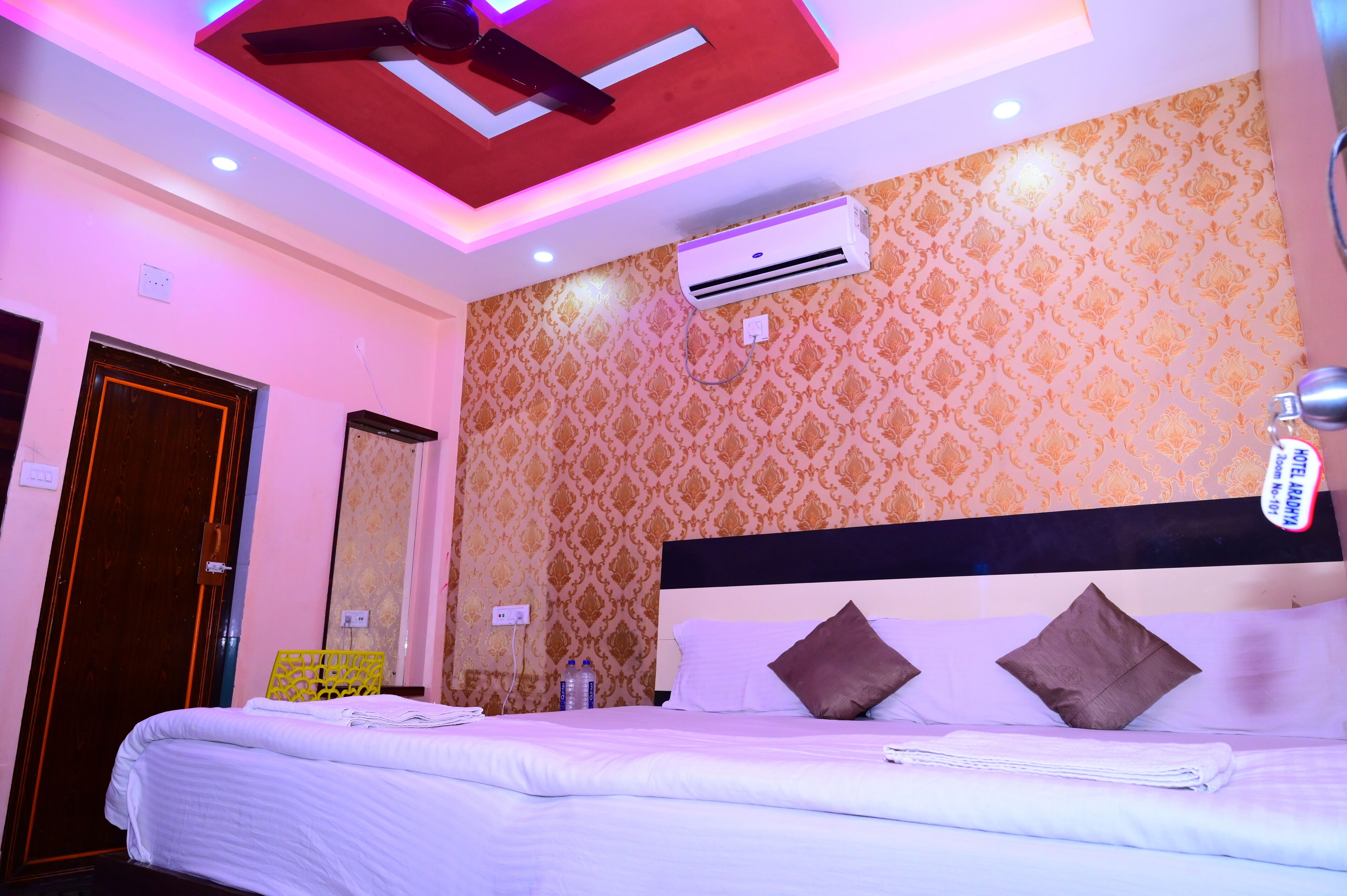 A hotel room with a bed, air conditioning unit, ceiling fan, and patterned wallpaper.