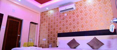 A hotel room with a bed, air conditioning unit, ceiling fan, and patterned wallpaper.