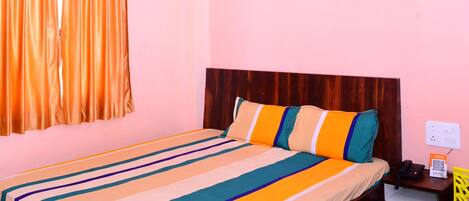 Um quarto com cama, ventilador de teto, cortinas, mesa de cabeceira e criado-mudo.