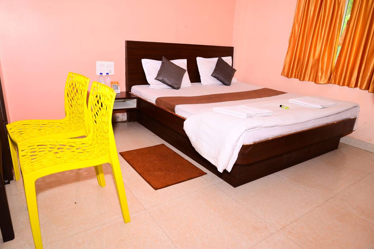 A hotel room with a bed, a nightstand, a yellow chair, and a brown mat.