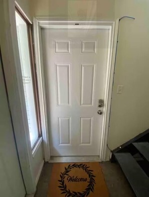 A white door with a rectangular panel design, a doormat with a wreath and the word "Welcome," and a staircase to the right. - Private 1 Bedroom Apartment in Lawton near Fort Sill (Lawton)