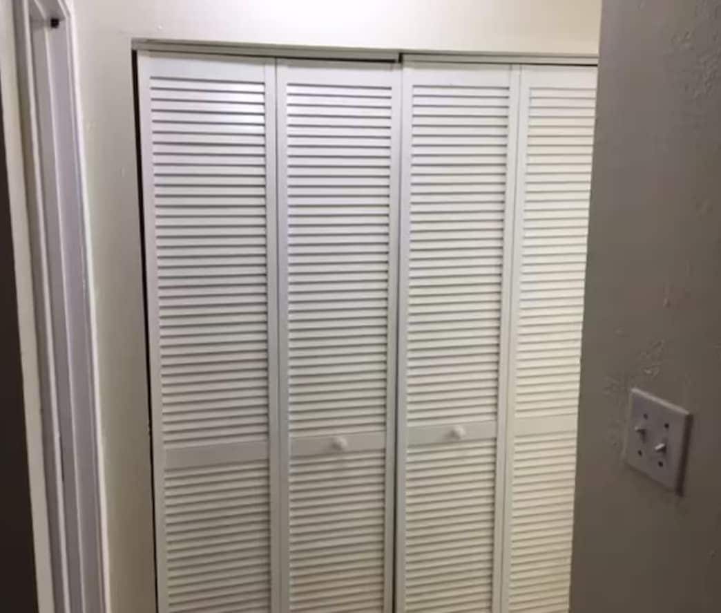 A white closet with horizontal louvered doors and a light switch on the wall.