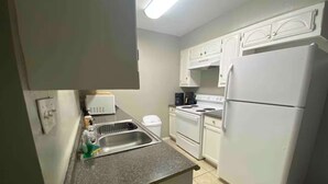 A compact kitchen with white cabinets, a built-in oven, a refrigerator, and a sink with a countertop.