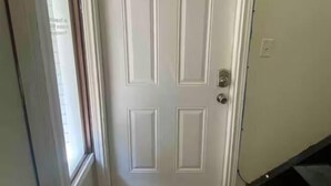 A white door with a rectangular panel design, a doormat with a wreath and the word "Welcome," and a staircase to the right.