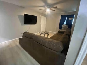 A living room with a brown sofa, a glass coffee table, and a flat-screen TV mounted on the wall. - Private 1 Bedroom Apartment in Lawton near Fort Sill (Lawton)