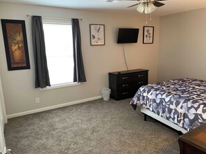 Ein Schlafzimmer mit Bett, Kommode, Fernseher und gerahmten Bildern an der Wand.