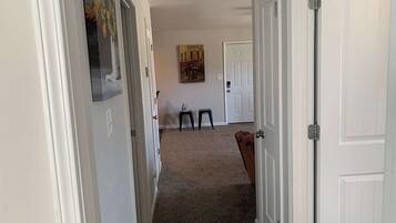A hallway with white doors, a carpeted floor, a small stool, and a painting on the wall.