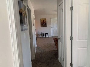 A hallway with white doors, a carpeted floor, a small stool, and a painting on the wall.