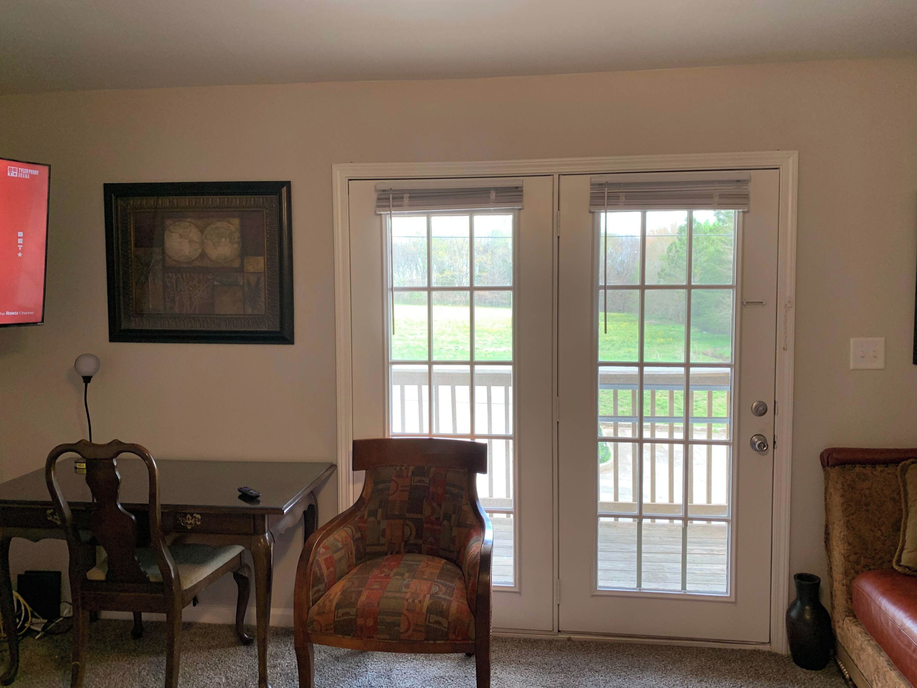 A living room with a wooden chair, a desk, a framed picture on the wall, and a sliding glass door leading to a deck.