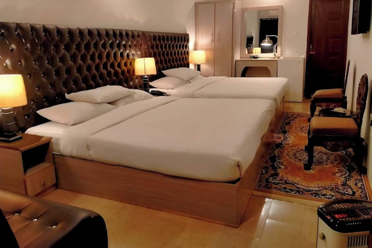 Une chambre d’hôtel avec un grand lit, deux tables de chevet avec des lampes, une tête de lit en bois, un bureau avec une chaise, un miroir et une armoire.