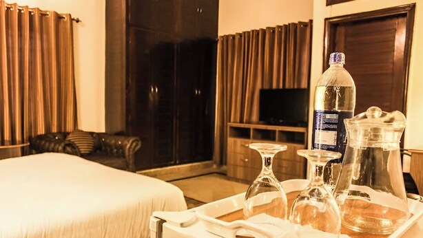 Une chambre d’hôtel avec un lit, une télévision, un plateau avec une bouteille, des verres et une carafe.