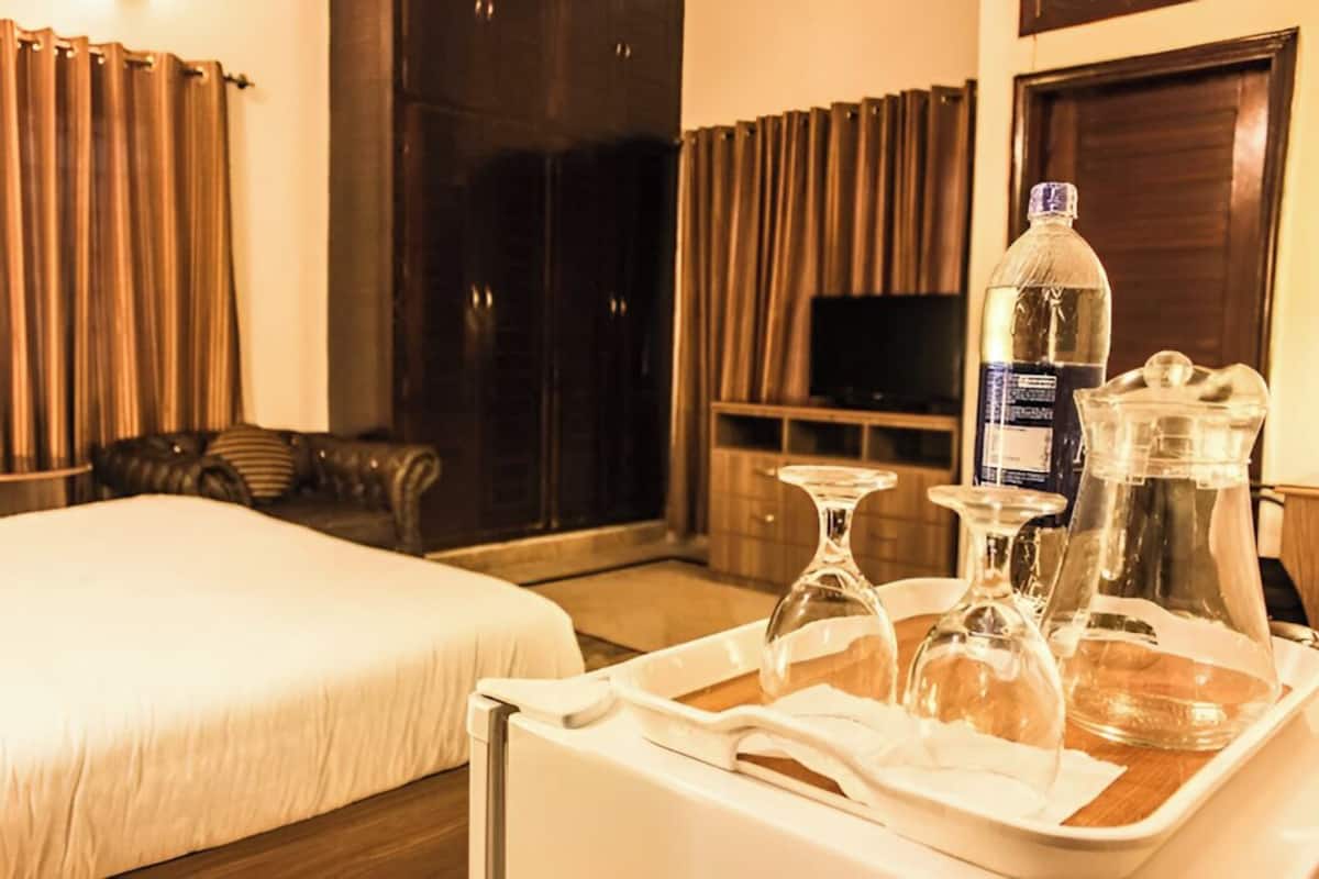 Une chambre d’hôtel avec un lit, une télévision, un plateau avec une bouteille, des verres et une carafe.