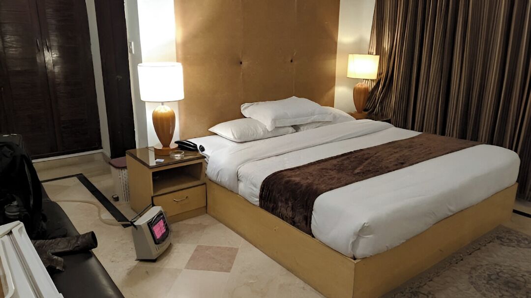 A hotel room with a large bed, bedside tables, lamps, a clock, and a dark-colored curtain.