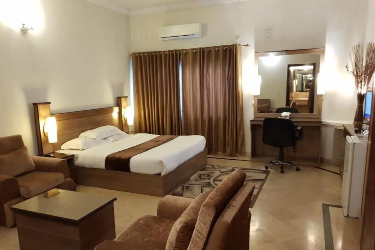 Une chambre d’hôtel comprenant un lit, deux fauteuils, un bureau et un miroir.