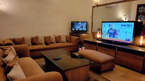 Un salon moderne avec un canapé marron, une table basse et un téléviseur diffusant une émission.