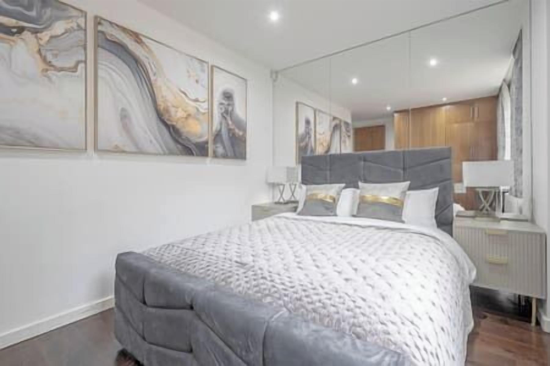 A modern bedroom with a large bed, a nightstand, a mirror, and abstract wall art.
