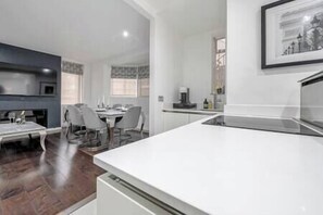 Een moderne keuken met witte kasten, een eethoek met een tafel en stoelen, en een open haard.