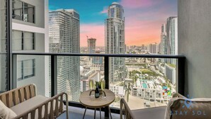 A balcony with a table, two chairs, and a view of high-rise buildings and a pool. - Modern  1BR Apartment with Pool (Miami)