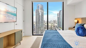 A modern bedroom with a city view, a large bed, a TV on the wall, and a wooden side table. - Modern  1BR Apartment with Pool (Miami)
