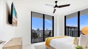 A modern bedroom with a large bed, a ceiling fan, and floor-to-ceiling windows offering a city view. - Downtown 2BR Oasis: Pool, Gym, Balcony Views (Miami)