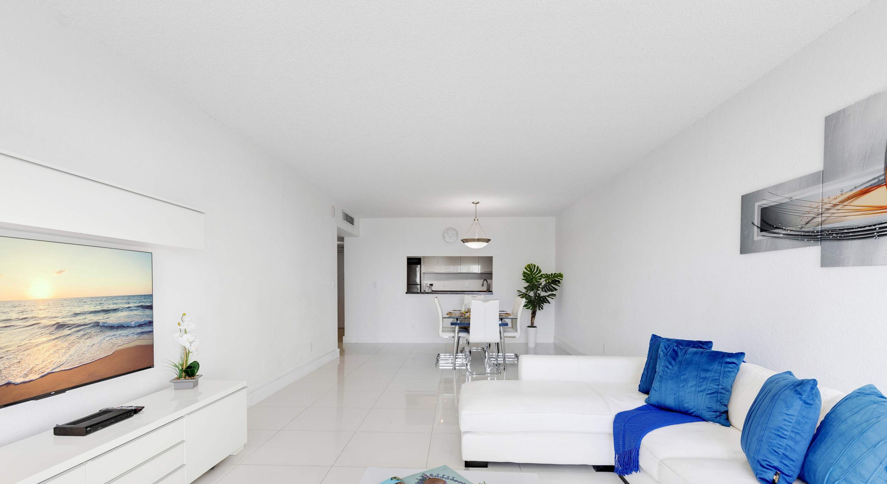 Uma sala de estar moderna com um sofá branco, uma TV de tela plana e um espaço de jantar com mesa e cadeiras.