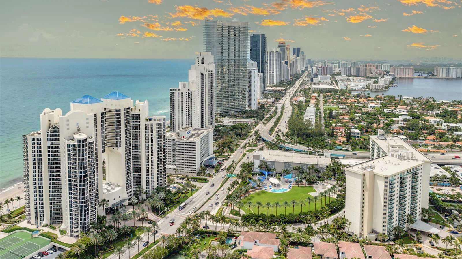 Un paysage urbain côtier avec de hauts immeubles, une marina et un grand parc au centre.