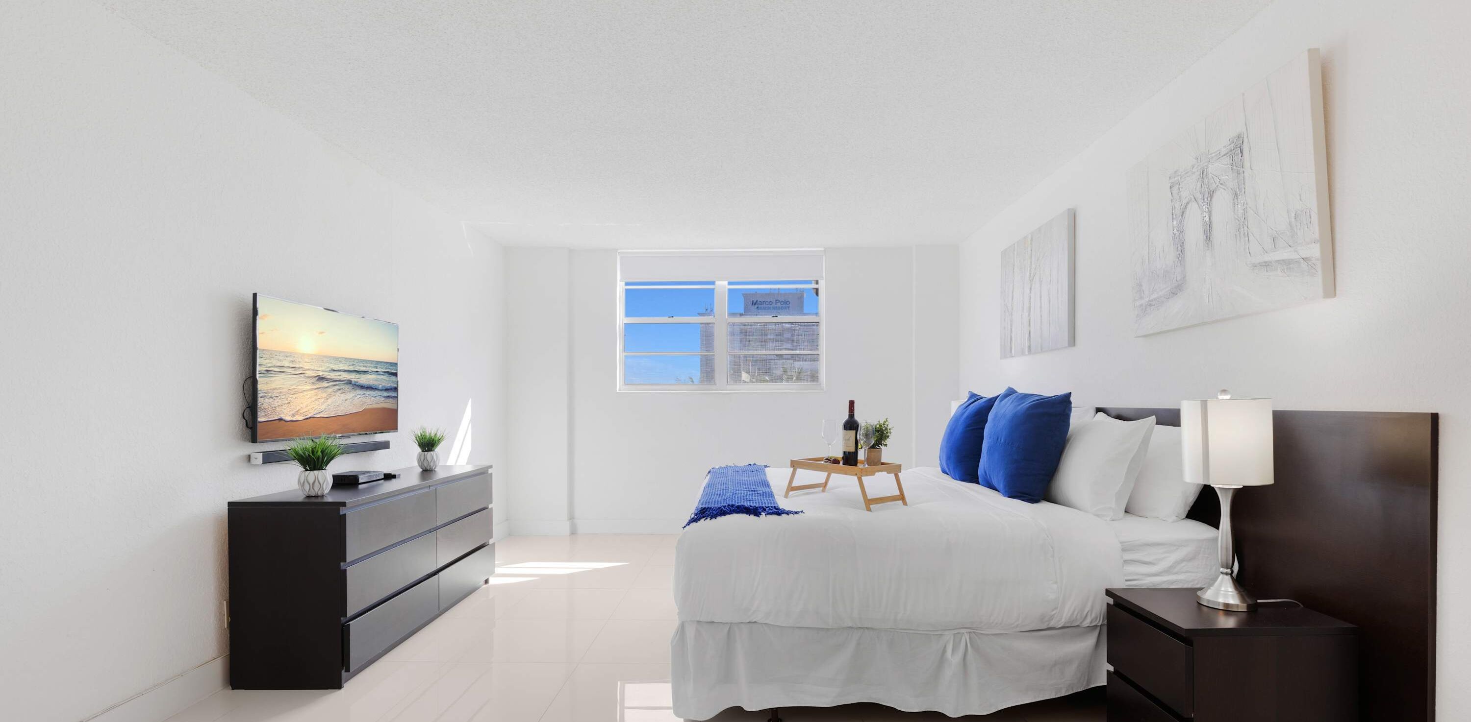 A modern bedroom with a bed, bedside table, lamp, and a television on a stand.