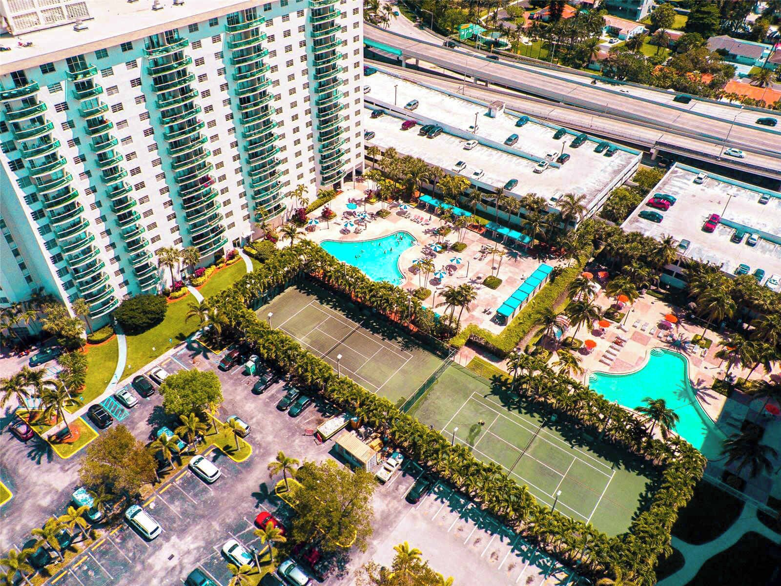 A high-rise hotel with a rooftop pool, tennis court, and multiple parking levels.
