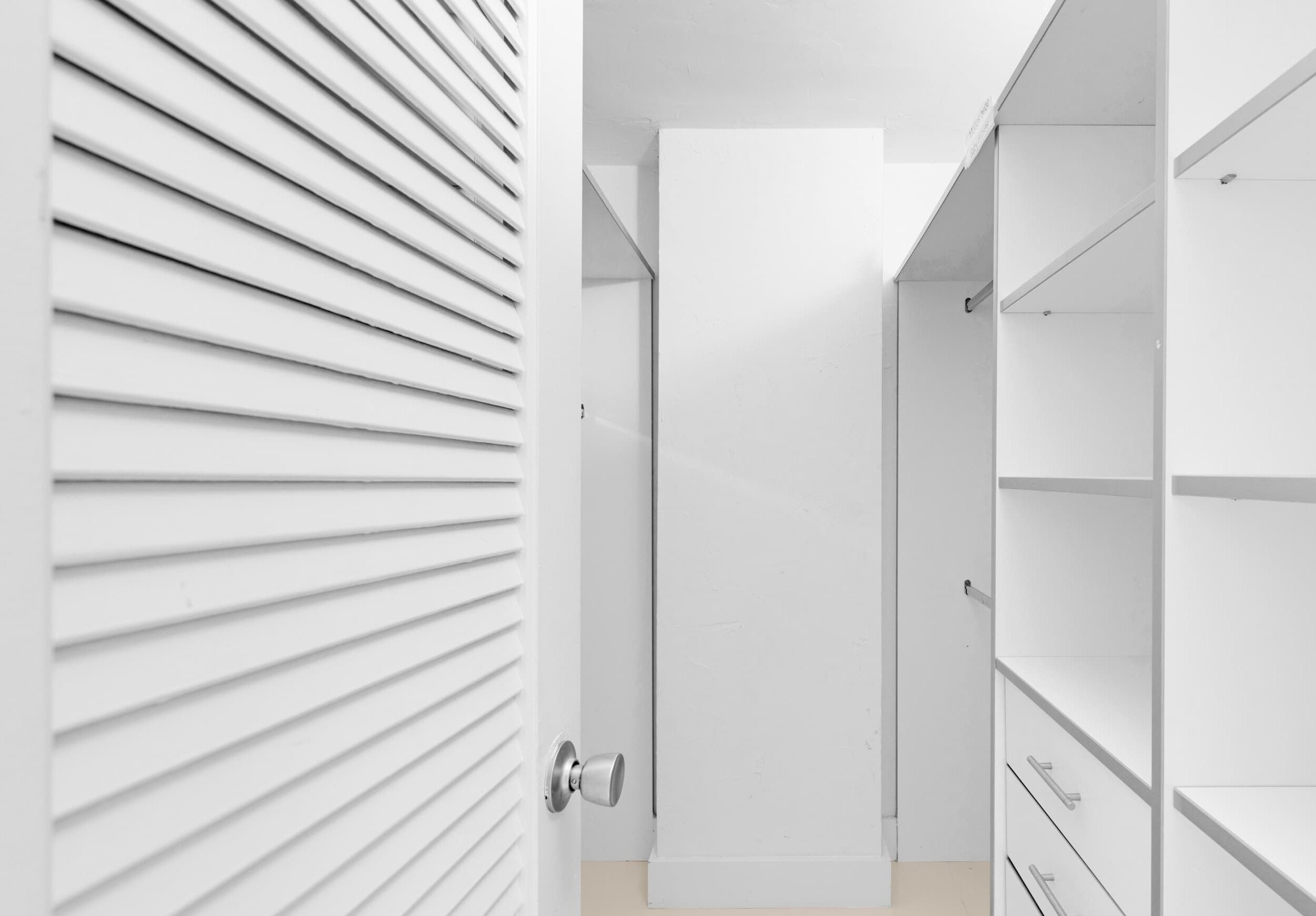 A modern, white closet with sliding doors and built-in shelves.