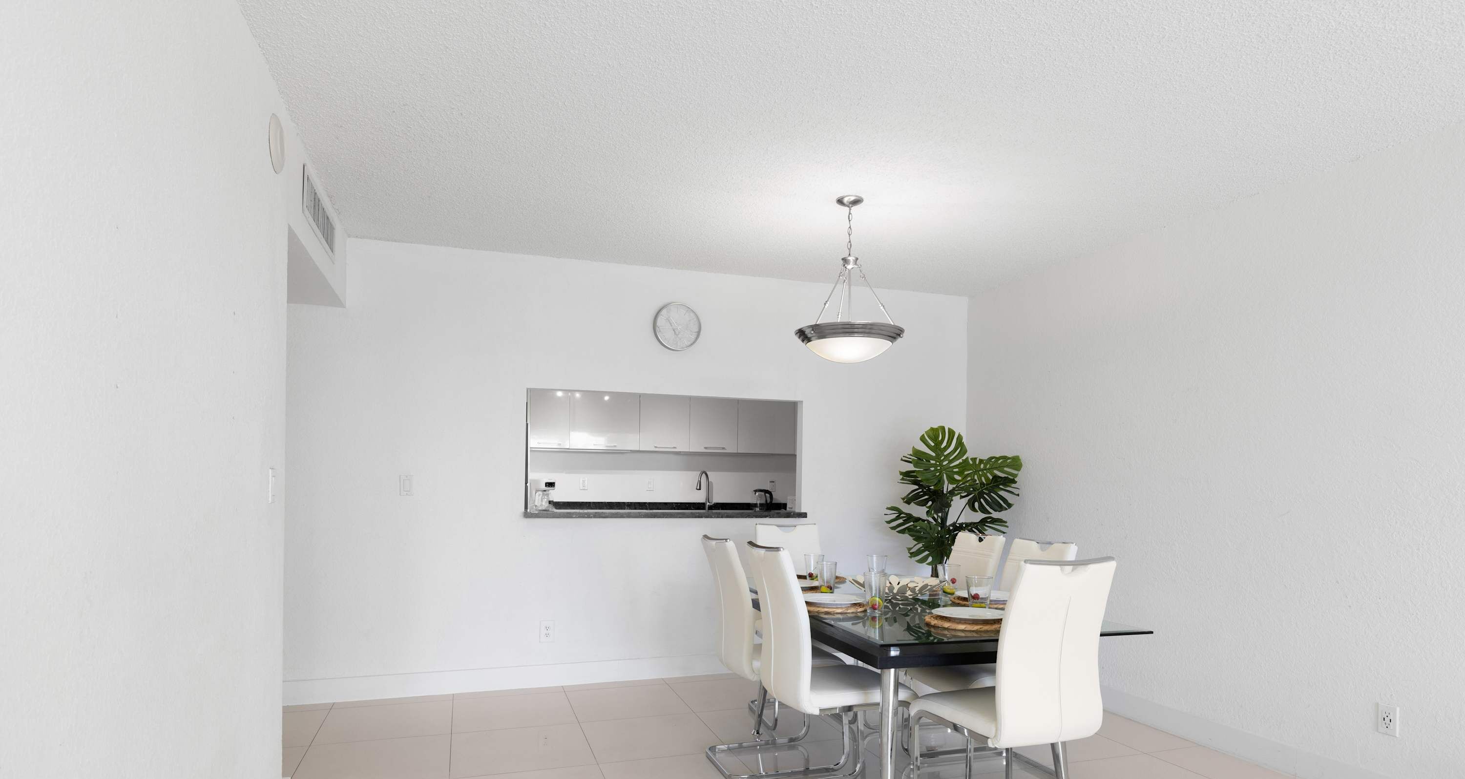 Un espace repas moderne avec une table noire, des chaises blanches, une plante en pot et une horloge au mur.