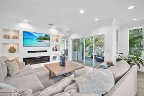 A modern living room with a large flat-screen TV, a fireplace, and a comfortable seating area. - Grove Walk Manor | 3BR Oasis in Coconut Grove (Miami)