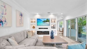 A modern living room with a large flat-screen TV, a sofa, a coffee table, and a fireplace.